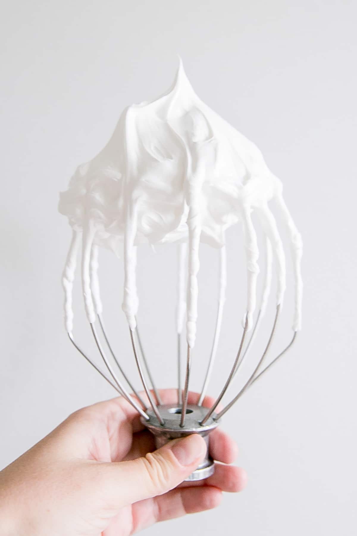 This old-fashioned 7 minute frosting recipe is light, delicious, and easy to make. A pure white frosting that's perfect for a variety of delicious desserts. | livforcake.com Holding a stand mixer whisk showing a stiff peak meringue.