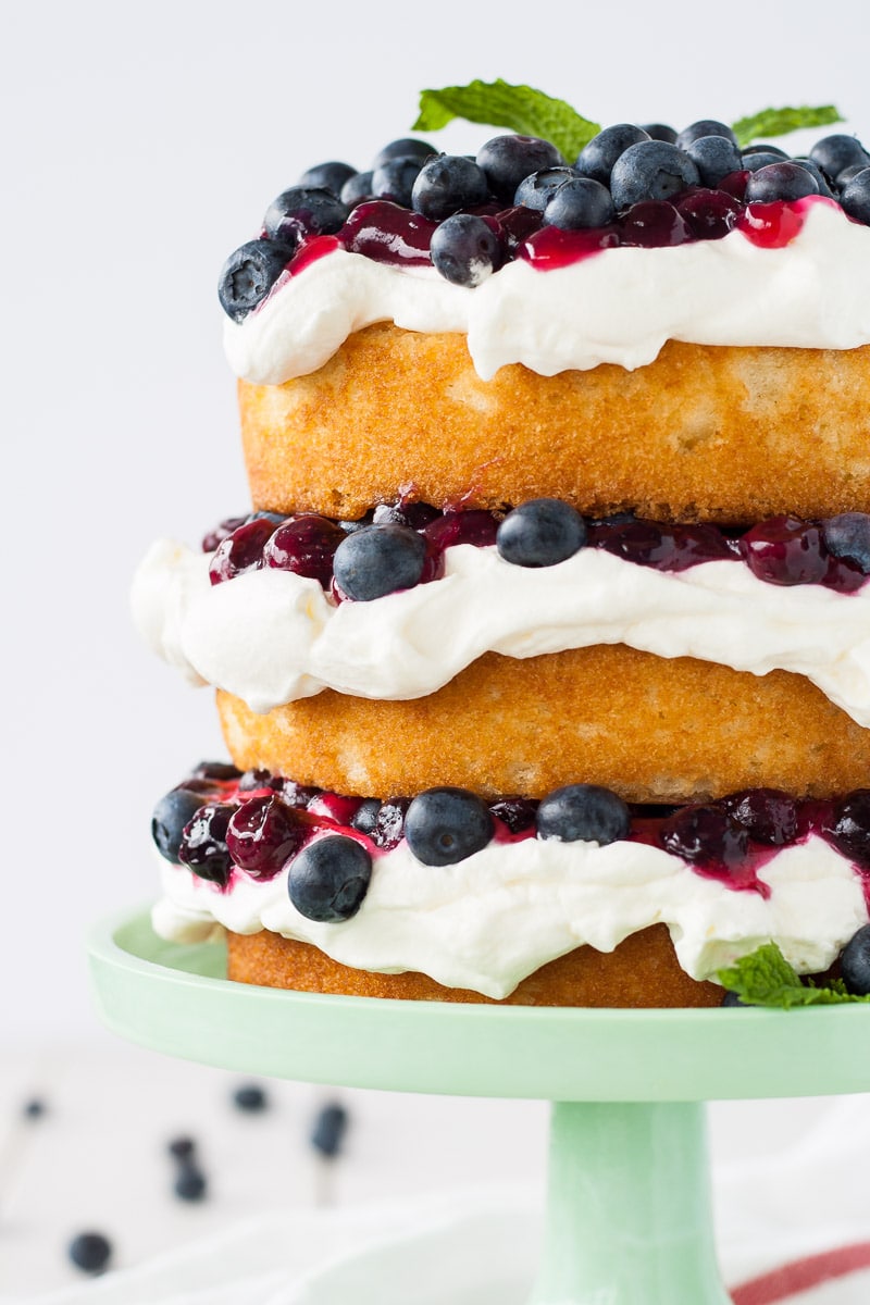 This Blueberry Shortcake Cake is the perfect light dessert for summer. Layers of vanilla cake, whipped cream, blueberry sauce, and fresh blueberries. | livforcake.com Close up shot of the side of the cake.