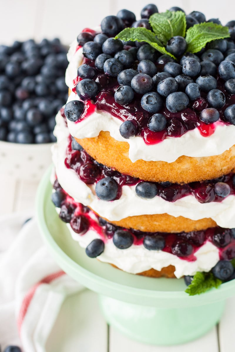 This Blueberry Shortcake Cake is the perfect light dessert for summer. Layers of vanilla cake, whipped cream, blueberry sauce, and fresh blueberries. | livforcake.com Angled shot of the top of the cake showing the fresh blueberries on top.