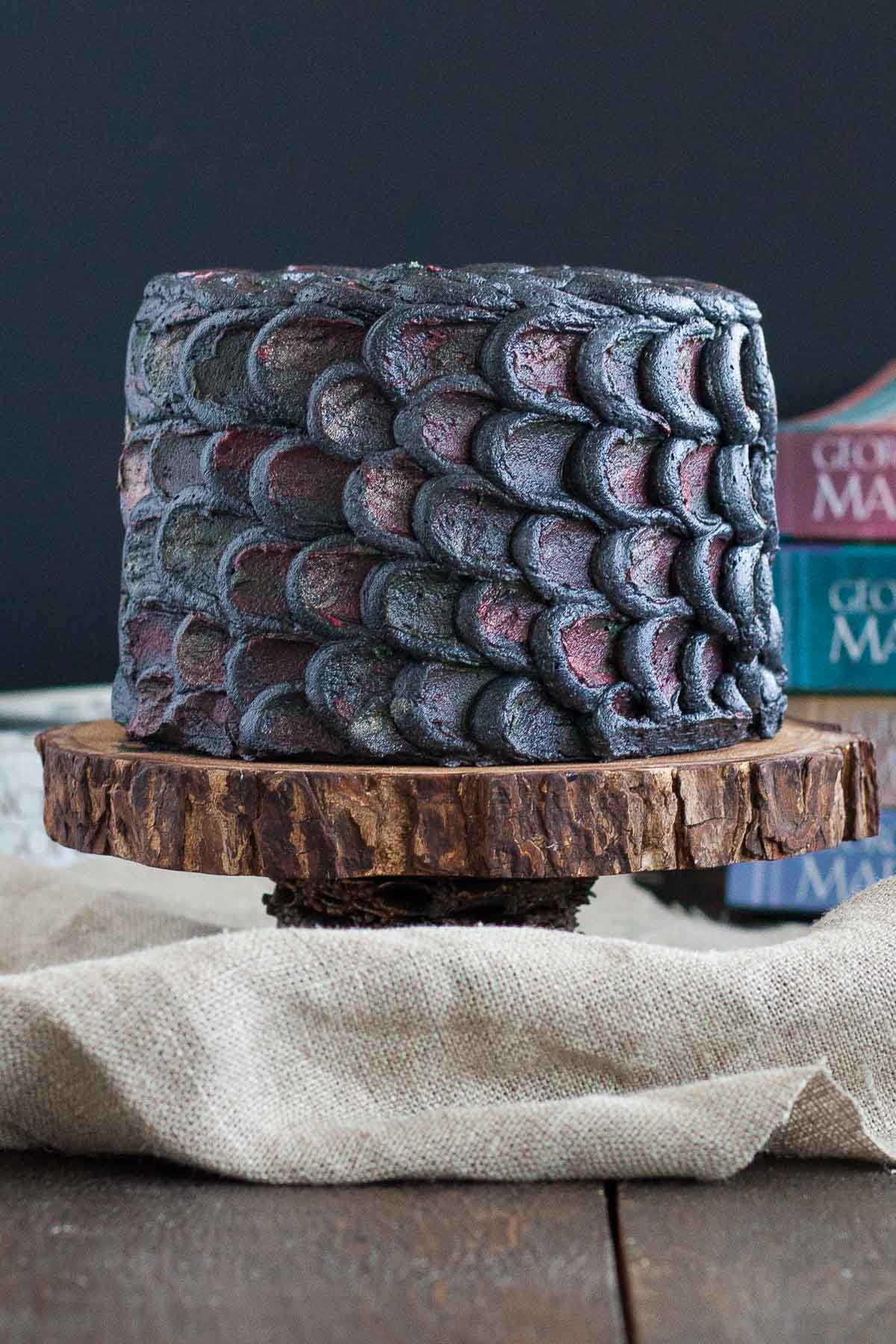 Cake decorated with dragonscales on a rustic cake stand with Game of Thrones books in the background.