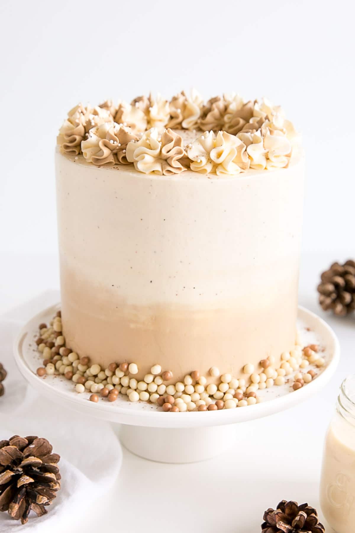 Eggnog Latte Cake! Transform a favourite holiday beverage into a decadent dessert with this Eggnog Latte Cake! Eggnog infused cake layers paired with eggnog and espresso buttercreams. | livforcake.com Slightly angled shot of the eggnog cake with pine cones in the foreground.
