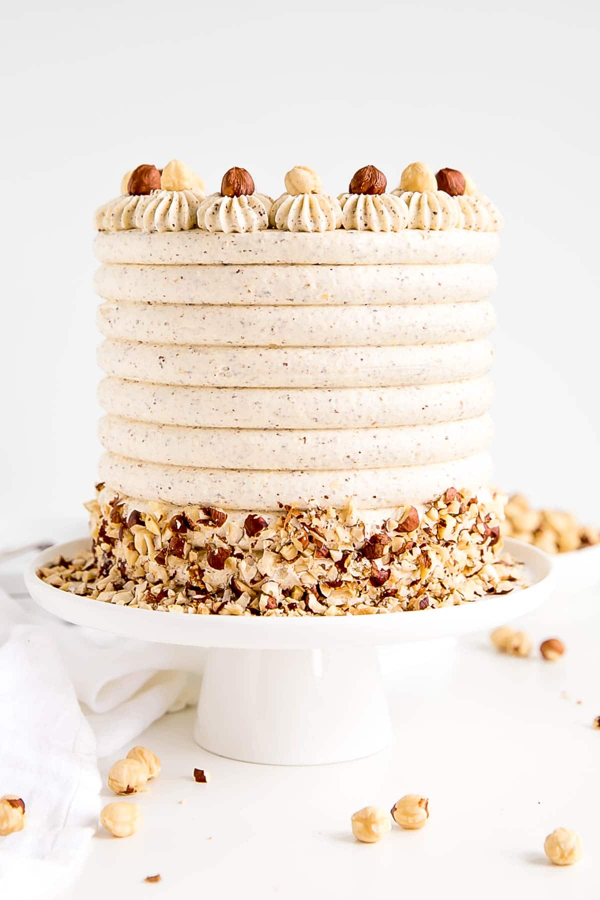 Cake on a white cake stand with a white cloth in the background.