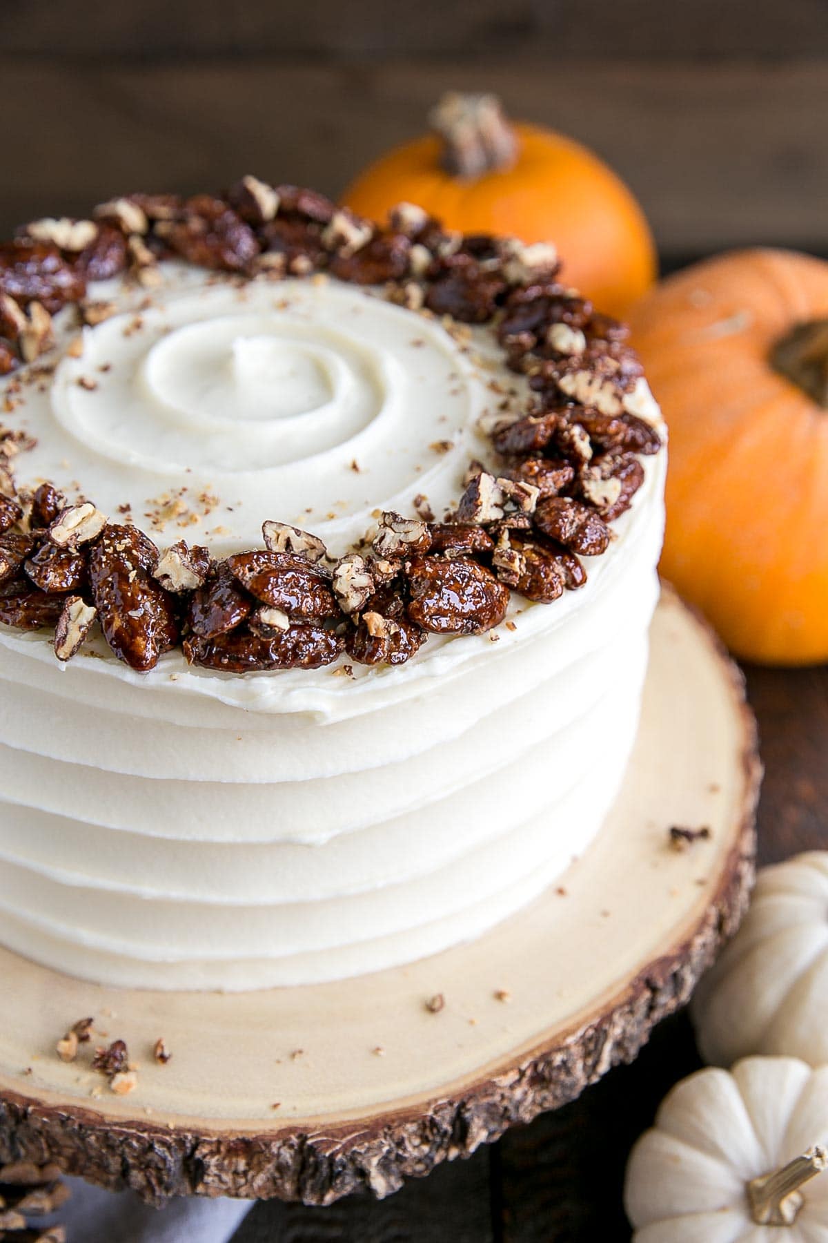 This pumpkin cake is perfect for Fall! Moist and delicious pumpkin cake layers with a tangy cream cheese frosting and crunchy candied pecans. | livforcake.com Close up of chopped pecans on top of the cake.